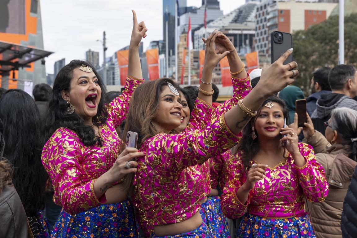Photo of women from the dance group Bollydance Dipti in pink costumes taking a selfie in a crowd