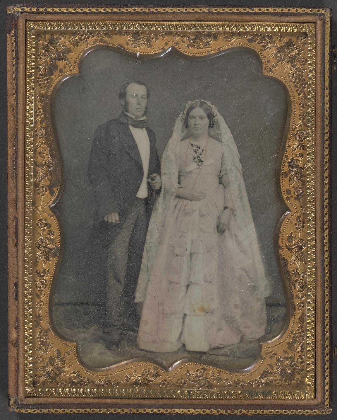 Old, black and white portrait of a young woman in a white dress and a man in a suit in an ornate gold frame