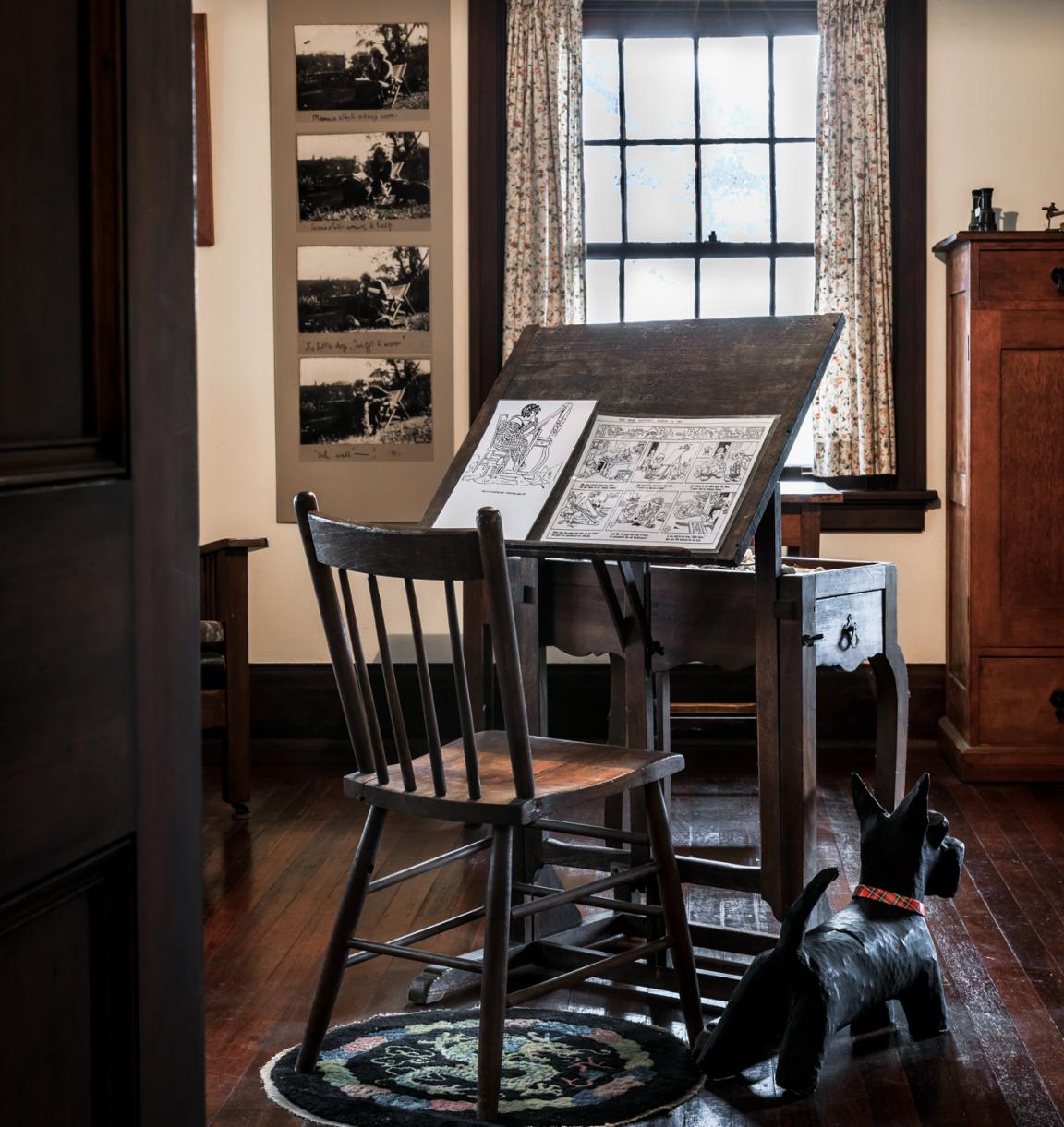 Easel, with two illustrated pages on it, and chair in May Gibbs' studio in Nutcote