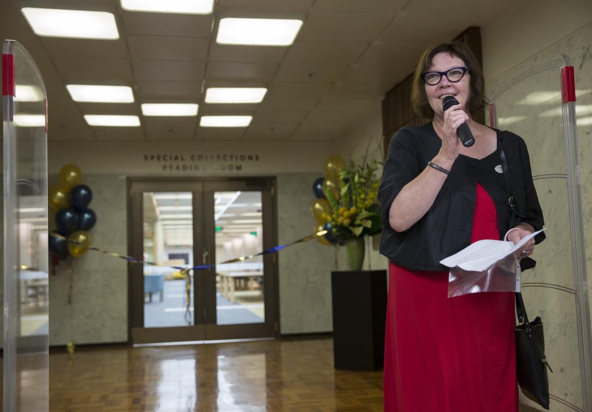 Woman, Margaret Burn, standing with a microphone in front of the Special Collections Reading Room, the opening of which is decorated with ribbons and balloons