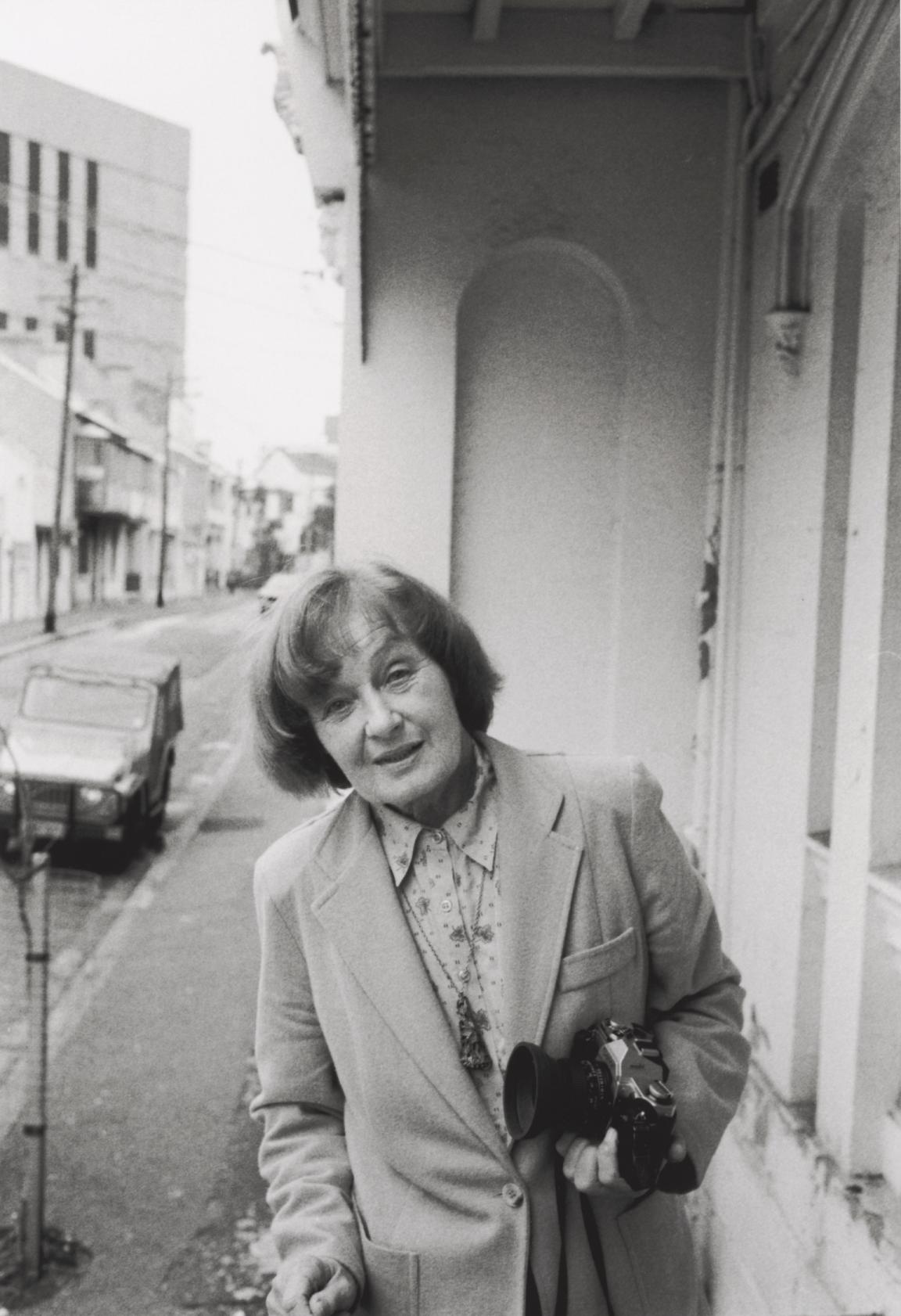 Black and white photo of Hazel de Berg holding a camera and half-smiling