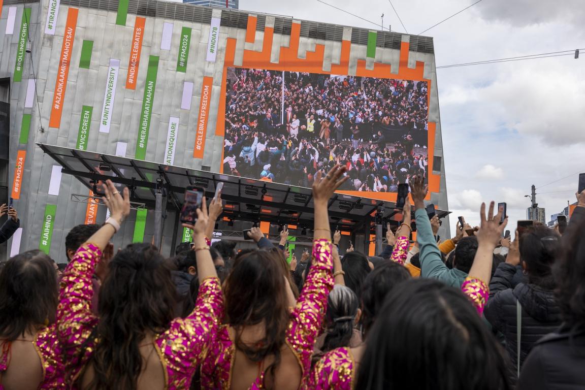 People from the Indian Australian community in cultural dress standing in front of a square building with their arms up