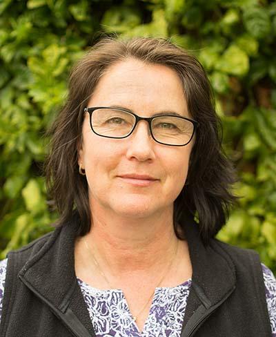 Photo of a woman with brown hair and glasses in front of a tree