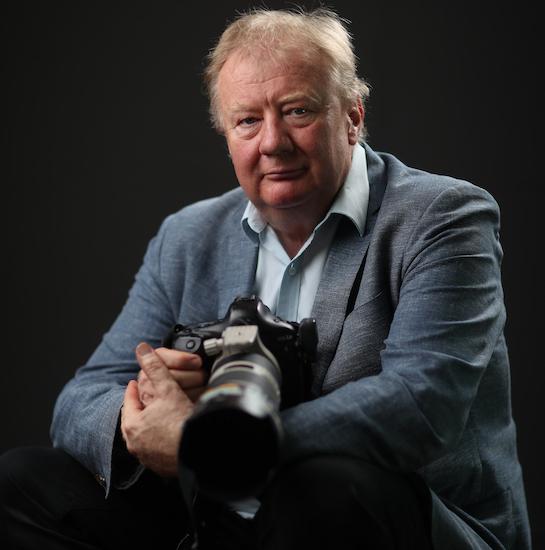 Mike Bowers sitting in a suit holding a camera