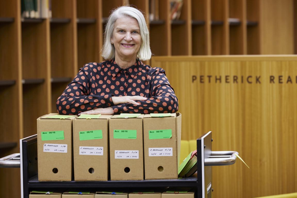 Woman, Ms Susan Wyndham, standing behind a trolley full of cardboard boxes of collection material in the Petherick Reading Room