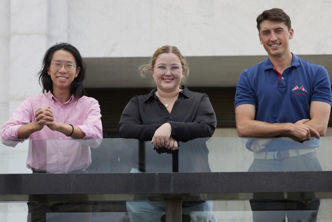 Two men and a woman leaning on the glass railing on the National Library podium and smiling