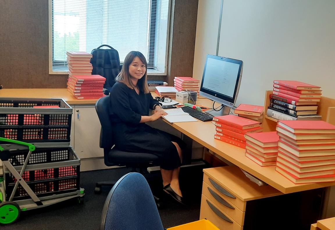 Dr Tin Kei Wong sitting at a desk surrounded by orange books