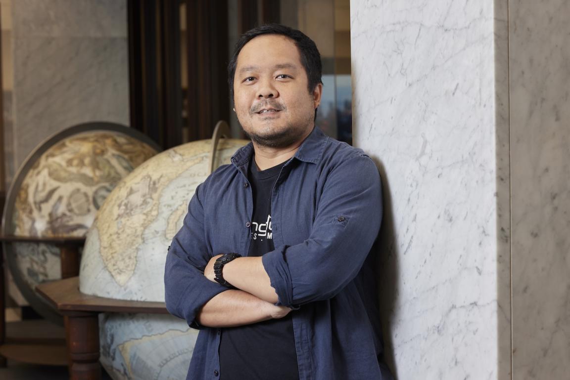 Michael Raditya leaning on a wall in the Main Reading Room and smiling