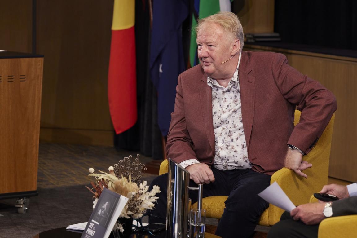 Mike Bowers sitting in a yellow armchair at the front of the theatre