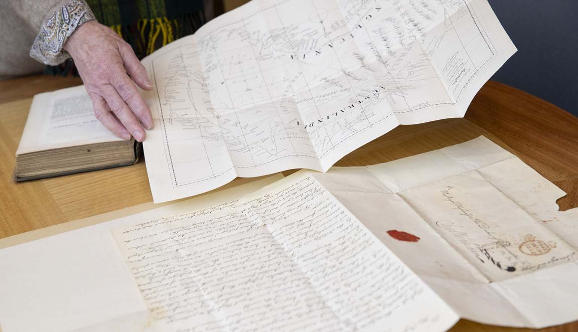 A handwritten document and a book on a desk with a hand holding a map above them