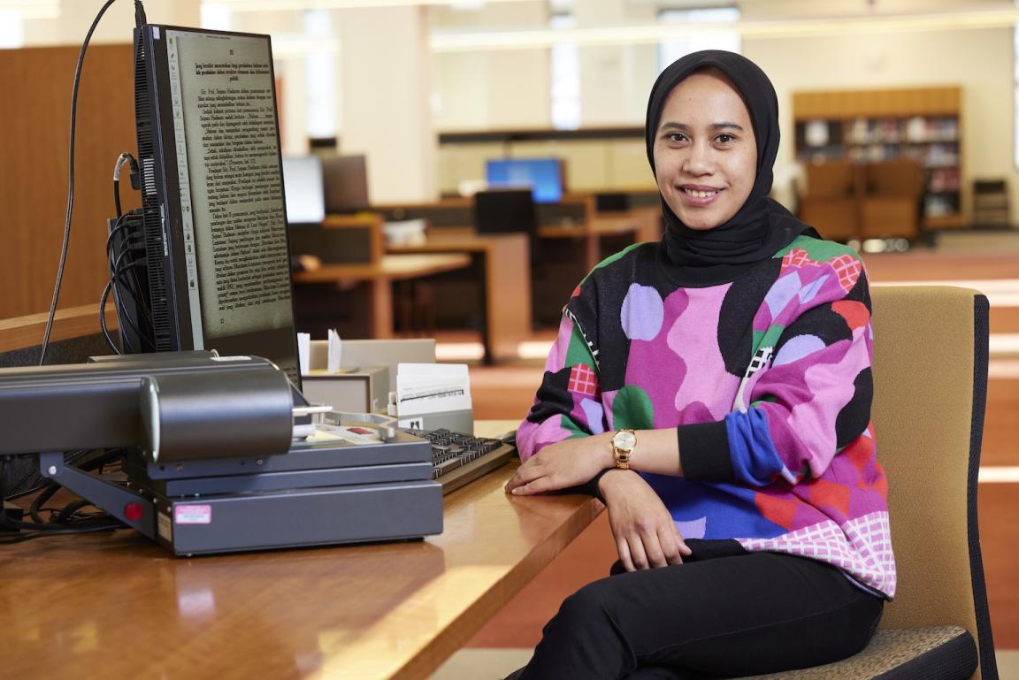 Dr Rafiqa Qurrata A'yun sitting at a computer in the Main Reading Room and smiling