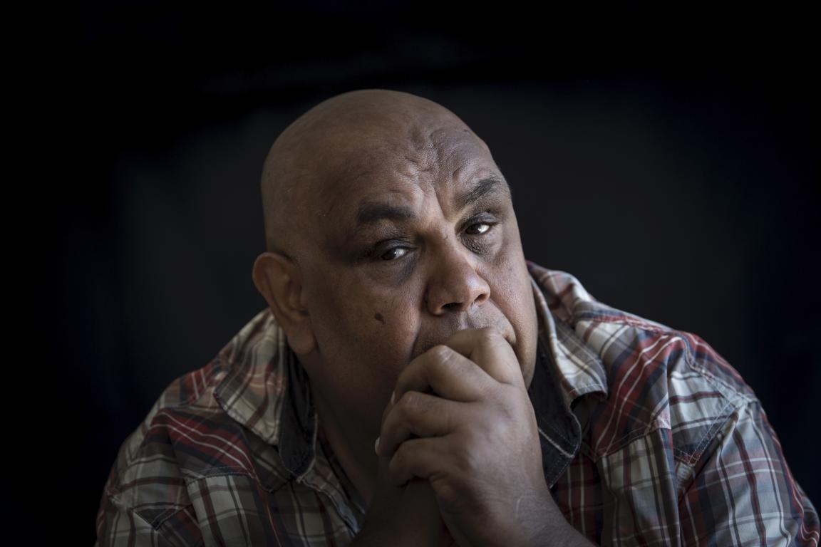 A color portrait of Kutcha Edwards, pensive, with his hand resting on his chin, looking directly at the camera.