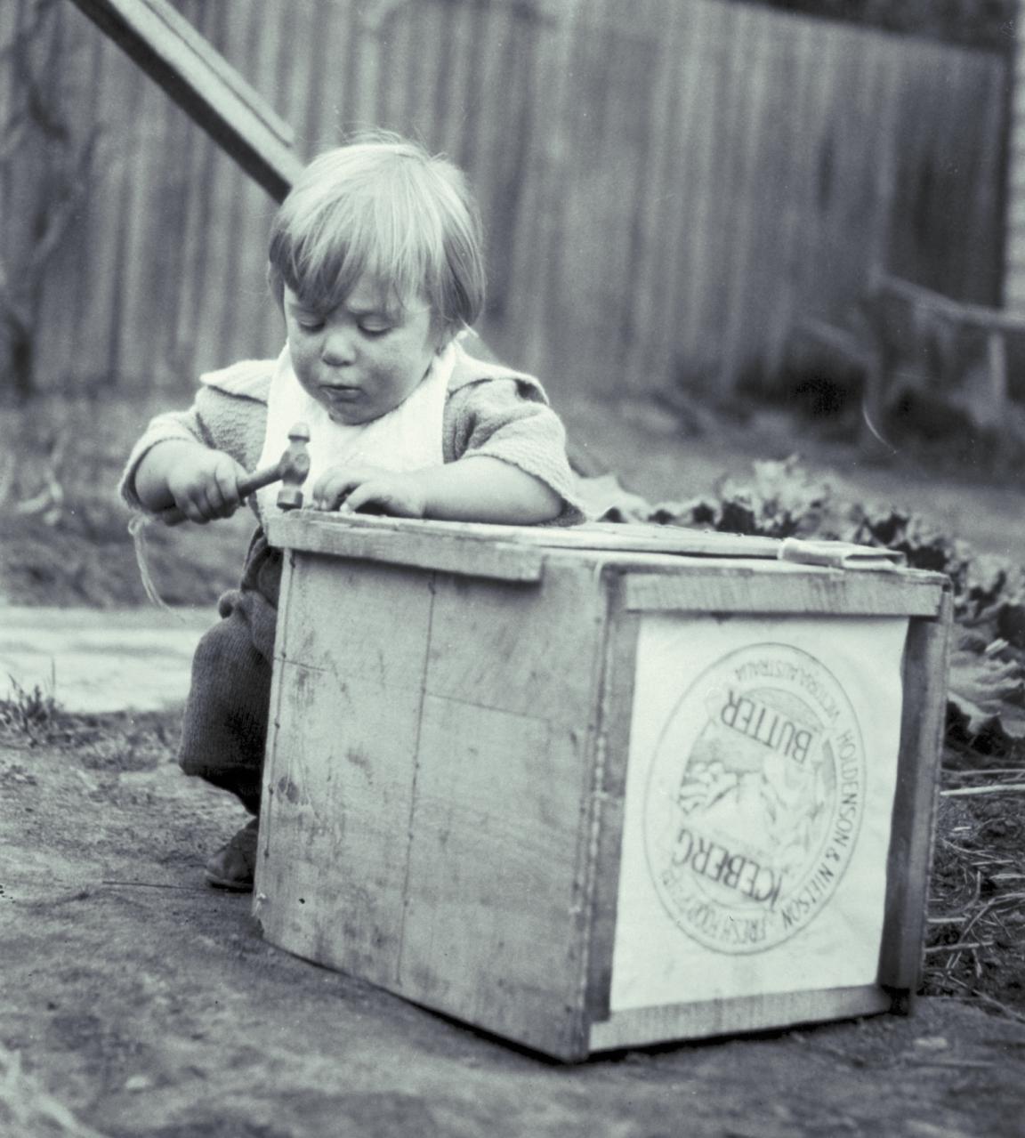 Black and white photo of a small child playing with a wooden box and a hammer