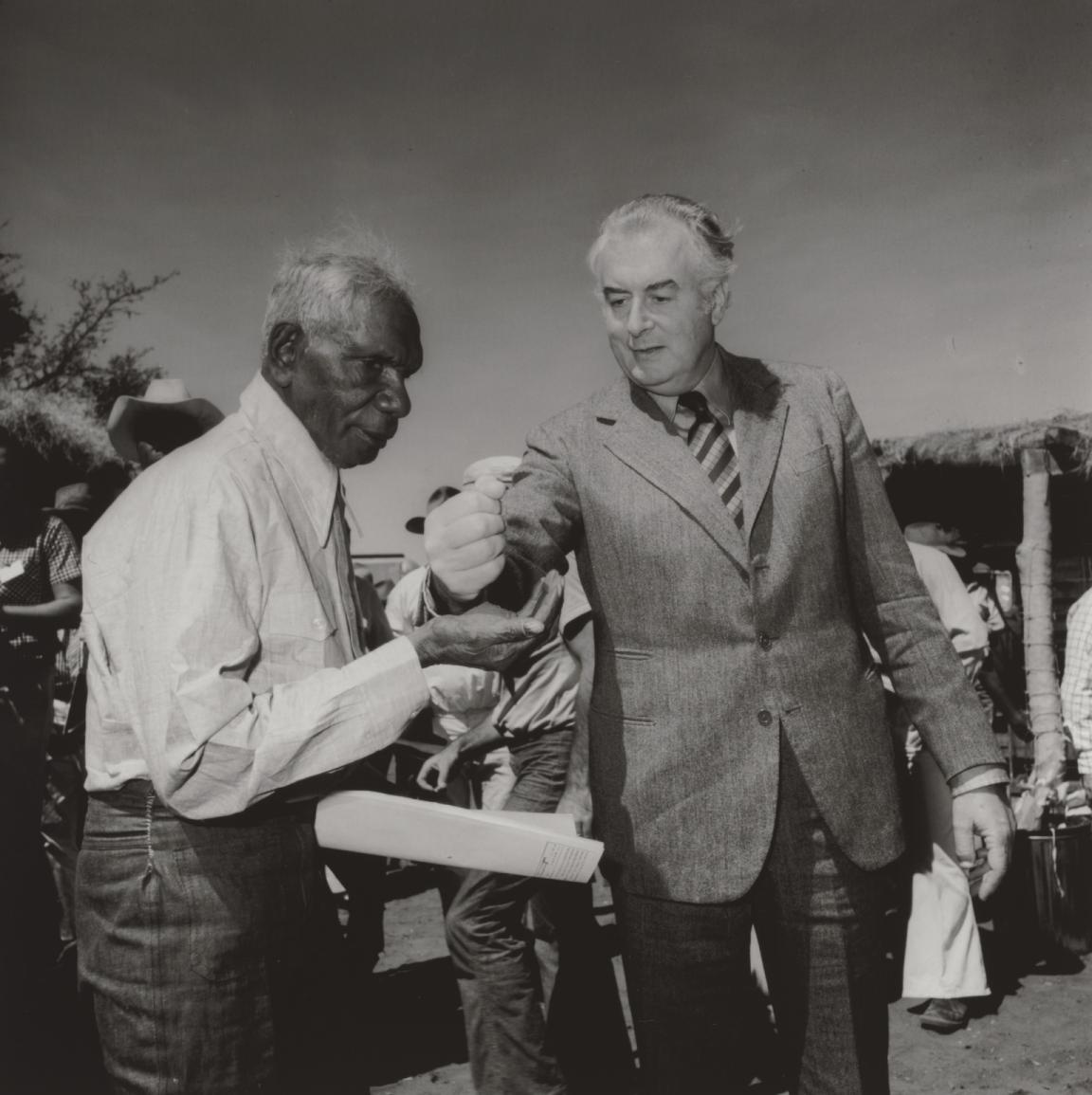 Black and white photo of Prime Minister Goufh Whitlam pouring soil into the hand of Gurindji Traditional Land Owner Vincent Lingiari at Wattie Creek