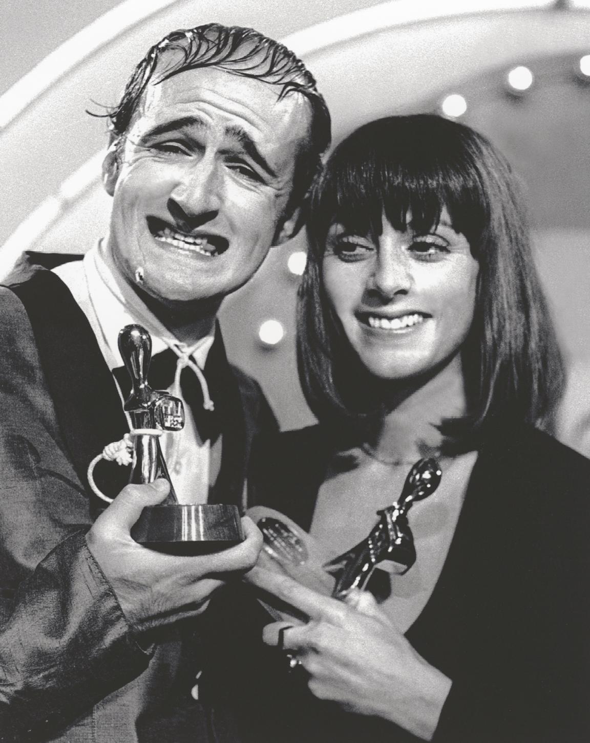 Black and white photo of Norman Gunston and Denise Drysdale smiling and holding up two Logie Awards trophies