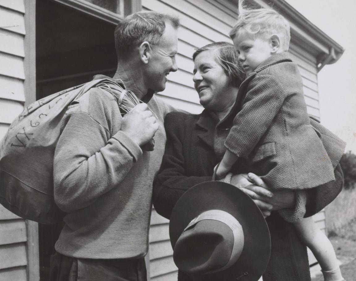 Man carrying a bag and woman holding a child embracing