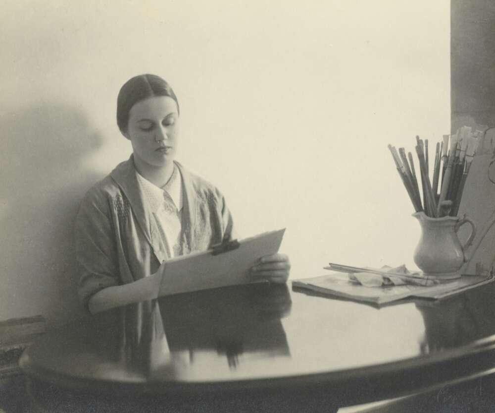 Portrait of Nora Heysen sitting at a desk and painting
