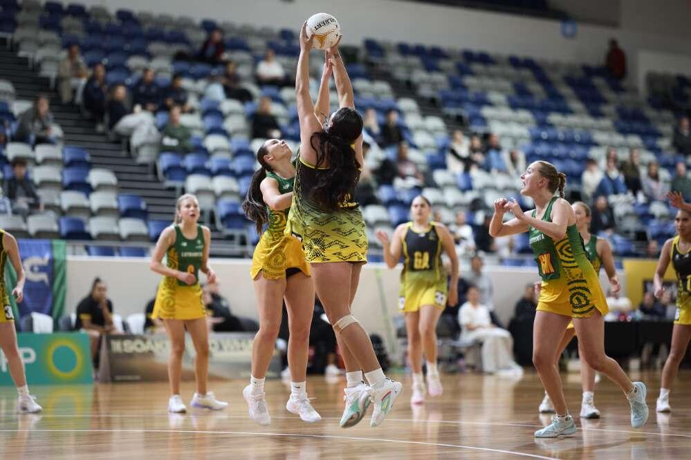 Action shot of a netball game as two women jump up to reach for the ball