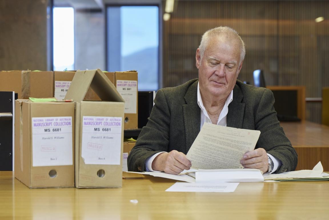 Man, Professor Robin Gerster, sitting at a table in the Special Collections Reading Room looking at manuscript material
