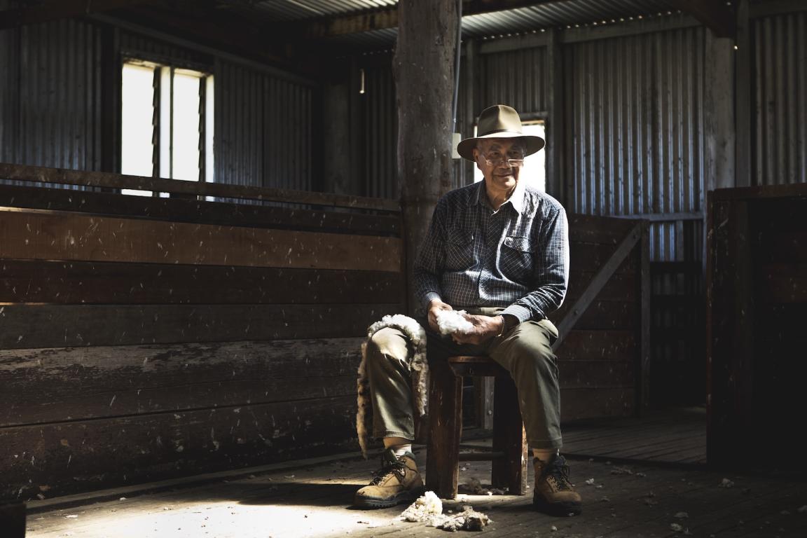 Photo of a man sitting, smiling, on a stool in a shearing shed