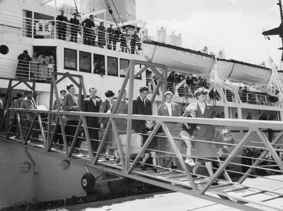 Black and white photo of men, women and children with suitcases getting of a large ship at an Australian port
