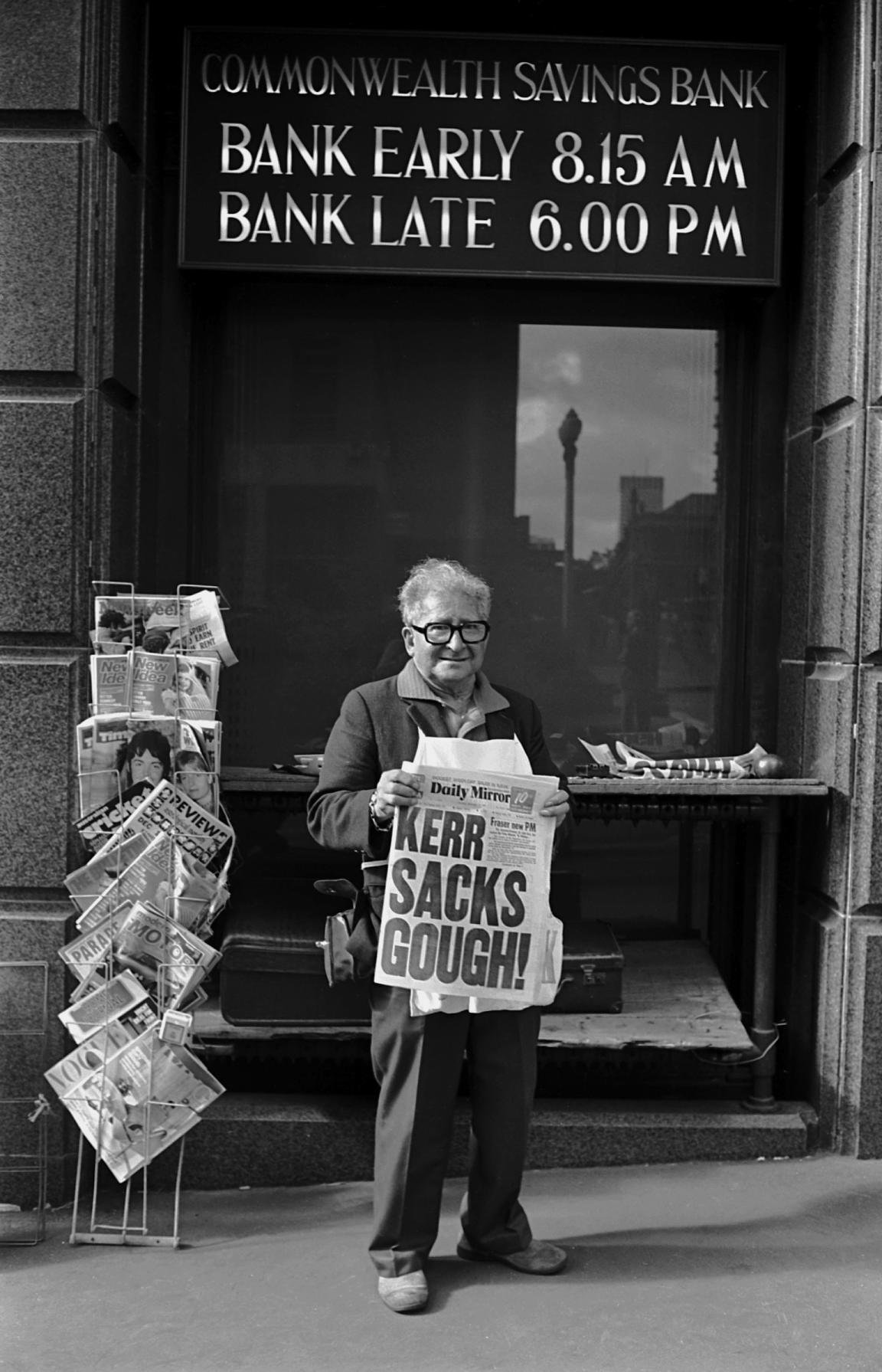 A black and white photography of a man holding a newspaper with the headline ‘Kerr sacks Gough’