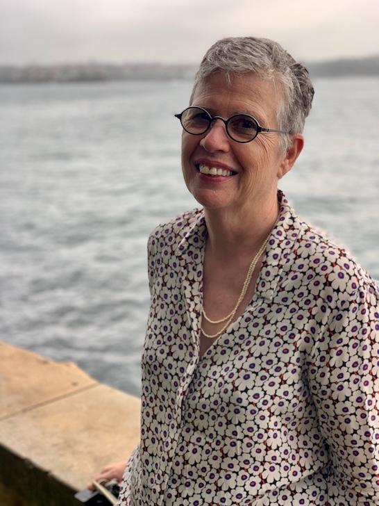 Woman, Ann Stephen, leaning on a rock wall near a body of water