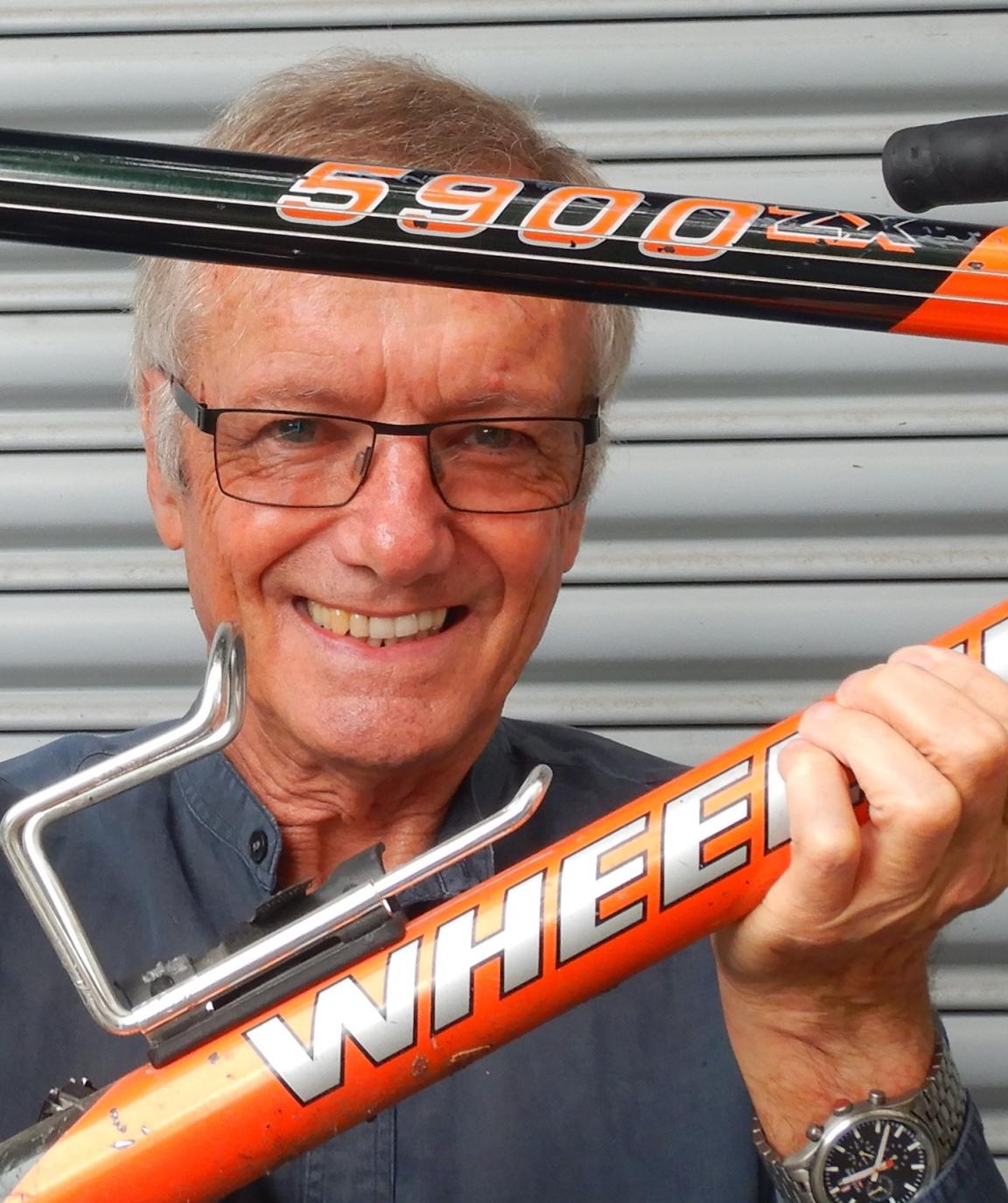 A man wearing glasses, his face pictured between the frame of a red and black bicycle