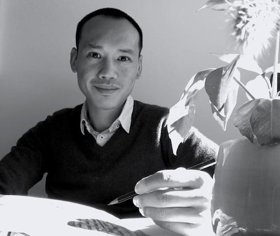 Black and white photo of man, Tull Suwannakit, smiling and holding a pencil
