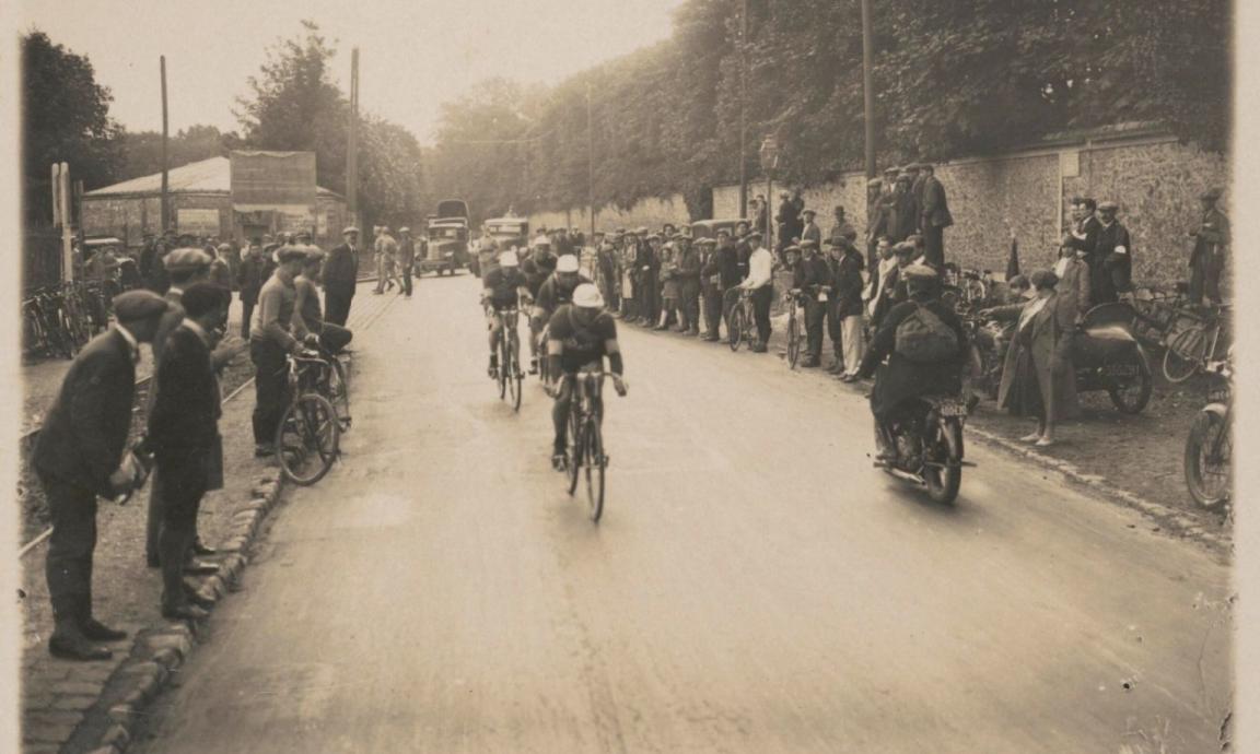 A black and white image of cyclists racing on a street lined by spectators