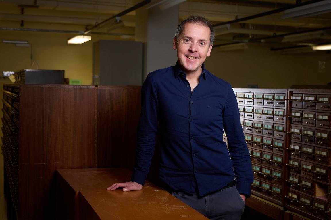 Prof. John Morrissey, 2025 National Library of Australia Stokes Fellow leaning on a table in one of the reading rooms. 