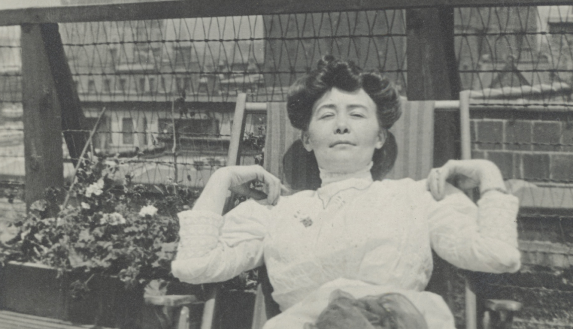 Detail of a black-and-white photograph of a woman reclining on a rooftop, dressed in a light-coloured Victorian-era dress, hands resting behind her head.