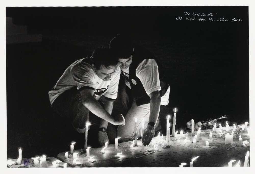 Two men kneel before rows of candles on the ground