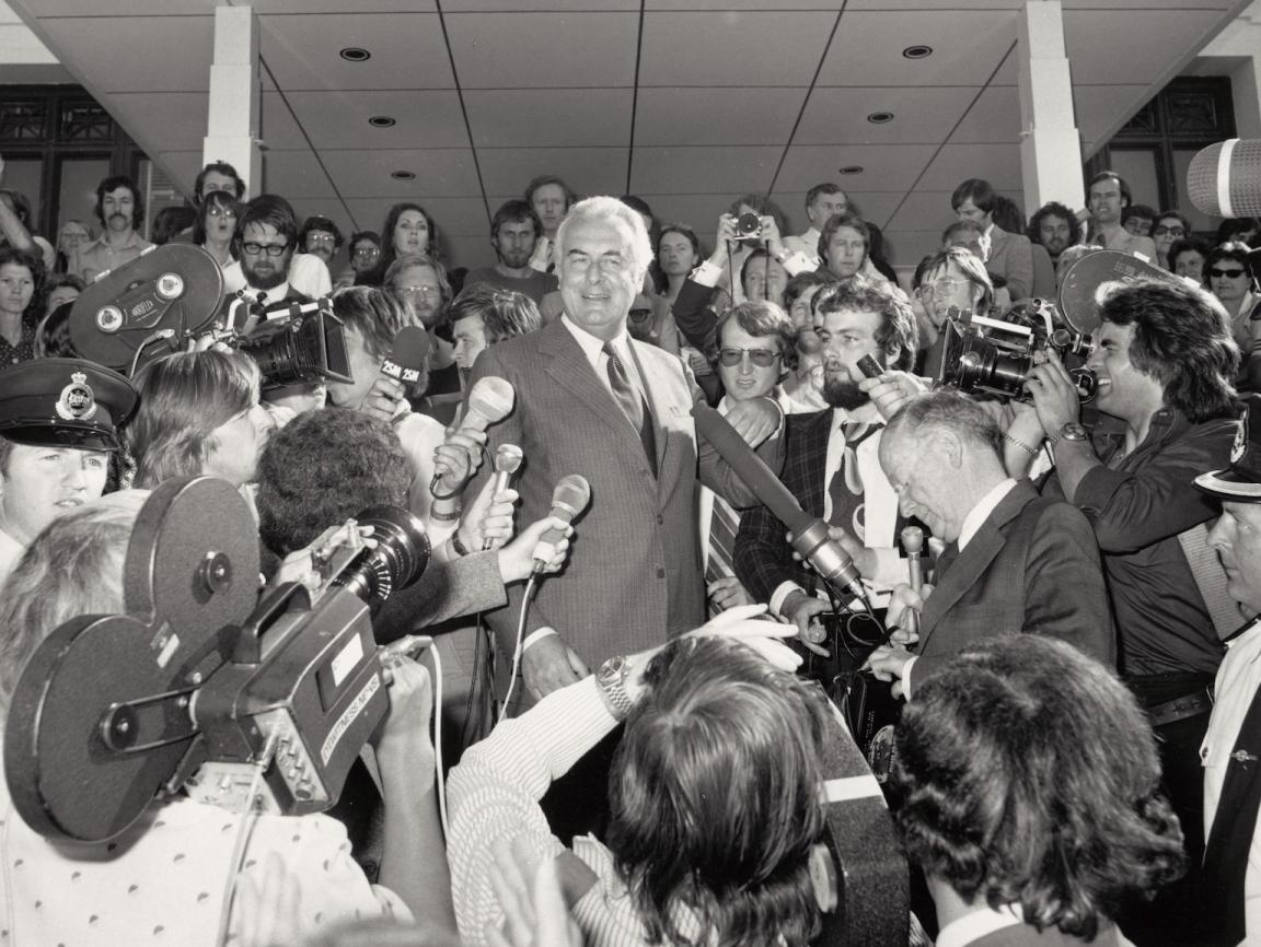 Black and white photo of Gough Whitlam speaking at Parliament House surrounded by reporters