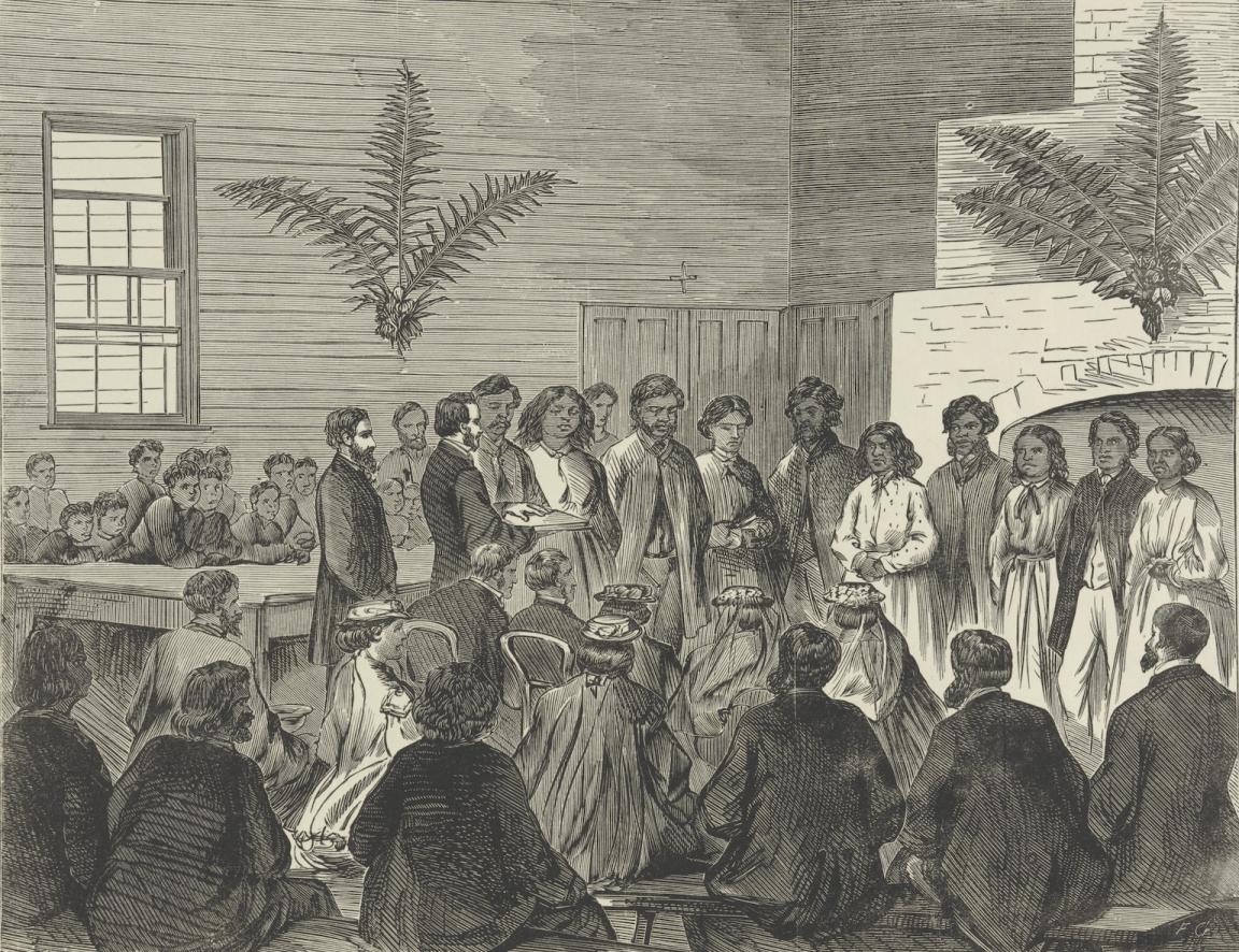 Black and white print of several First Nations people standing in a group, with a man reading from a book in front of them, and several people sitting and watching