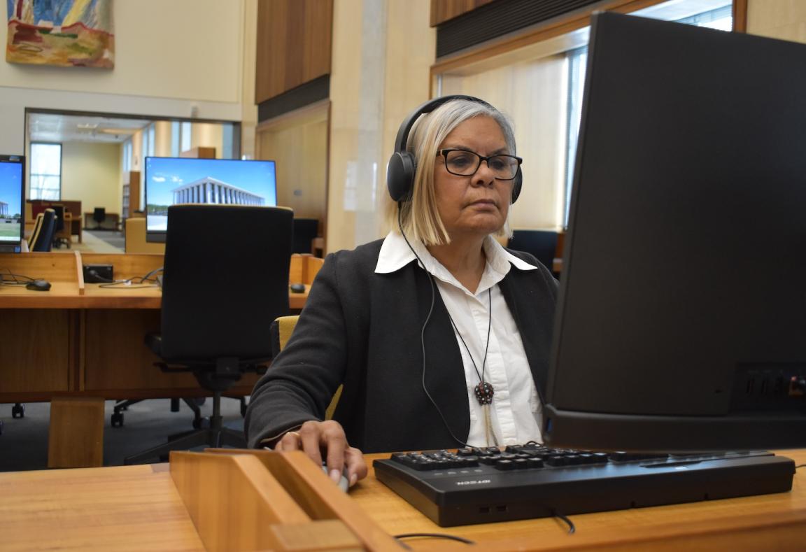 Wirangu Elder Sandra Miller sitting at a computer in the Main Reading Room wearing headphones and listening to an oral history recording