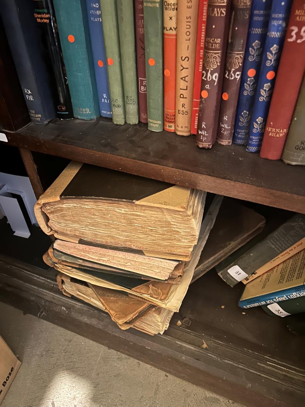 Two shelves of a bookcase. On the top shelf the spines of numerous books are visible. On the lower shelf there is several large, old books stacked sideways.
