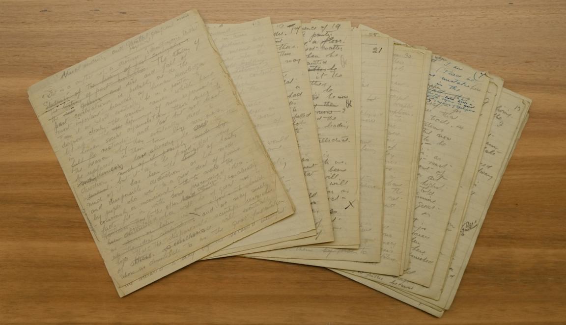 Old, thin pieces of paper with handwritten notes spread in a fan shape on a wooden table