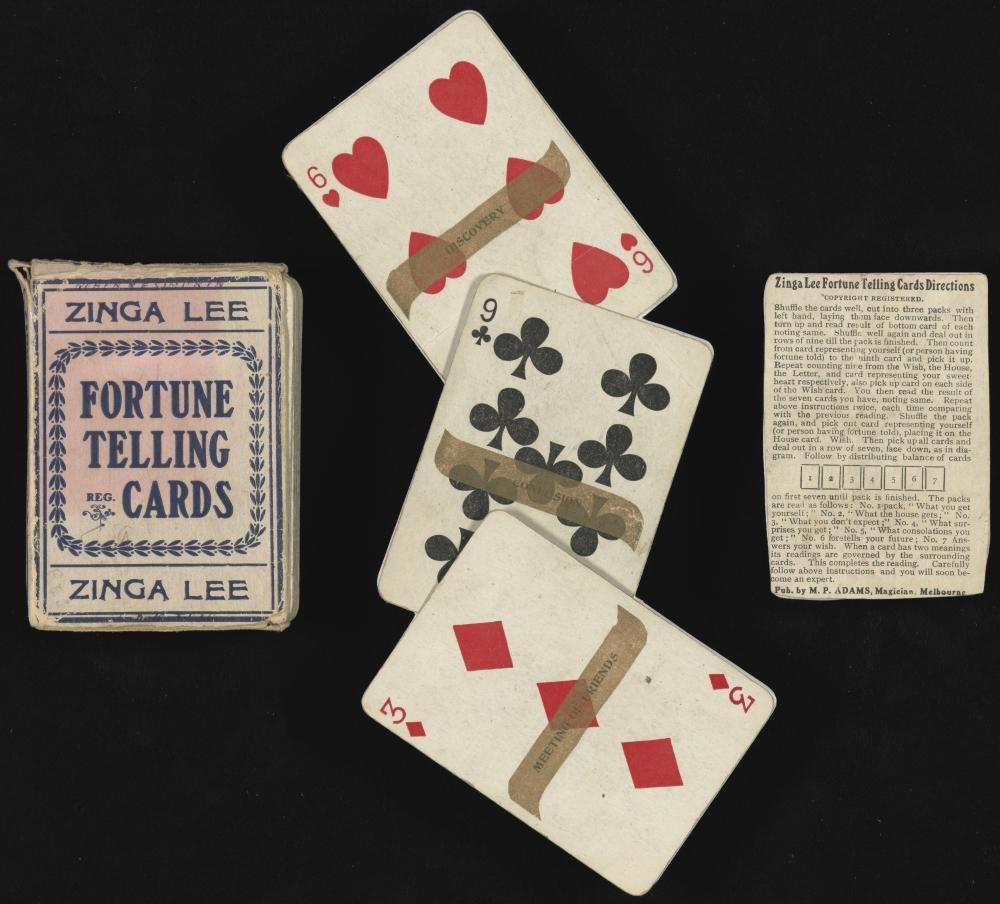 Three objects lie across this image on a black background. A card box, three playing cards with fortunes written on them, and an instruction sheet.
