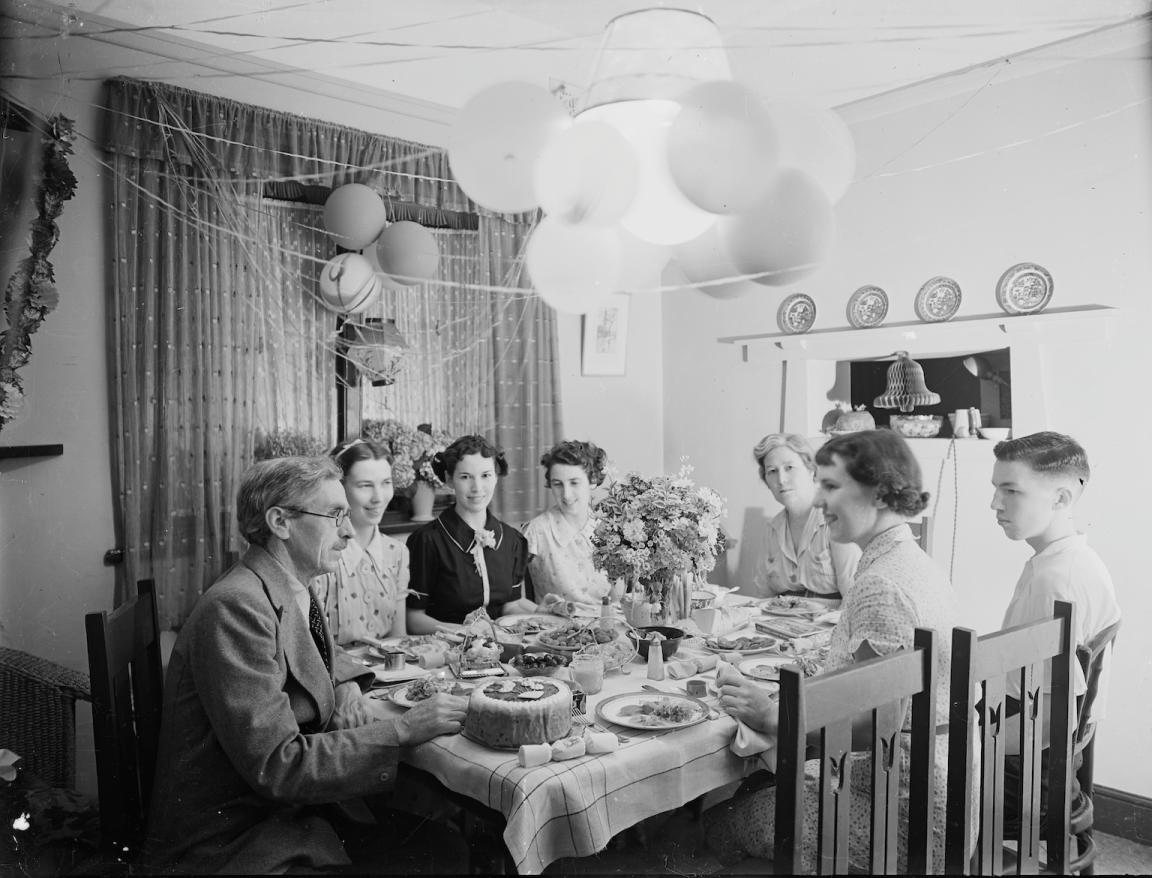 Black and white photograph of a family sitting around a dining table enjoying a Christmas meal with cake and decorations
