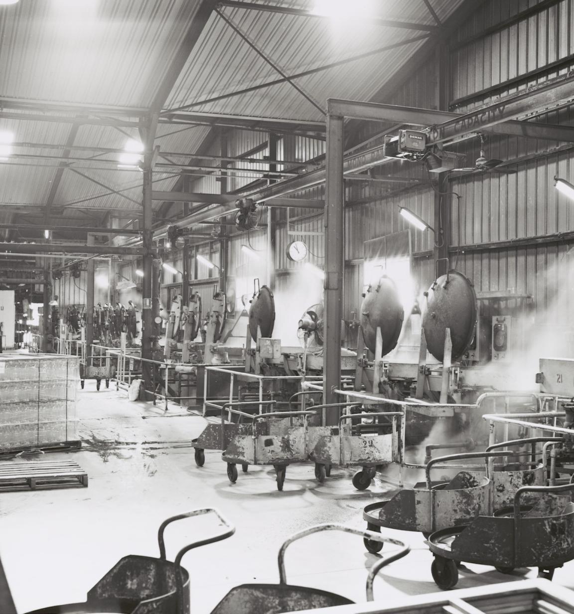 Black and white photo of a factory floor lined with steaming pressure cookers.