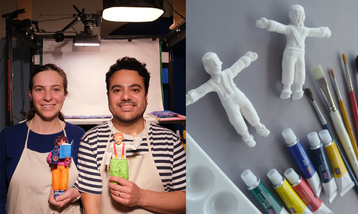 A woman and man wearing aprons and holding colourful maquettes, pictured alongside unpainted maquettes and paints and paintbrushes