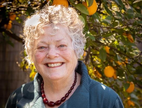 Woman, Sylvia Martin, smiling and standing in front of a hedge