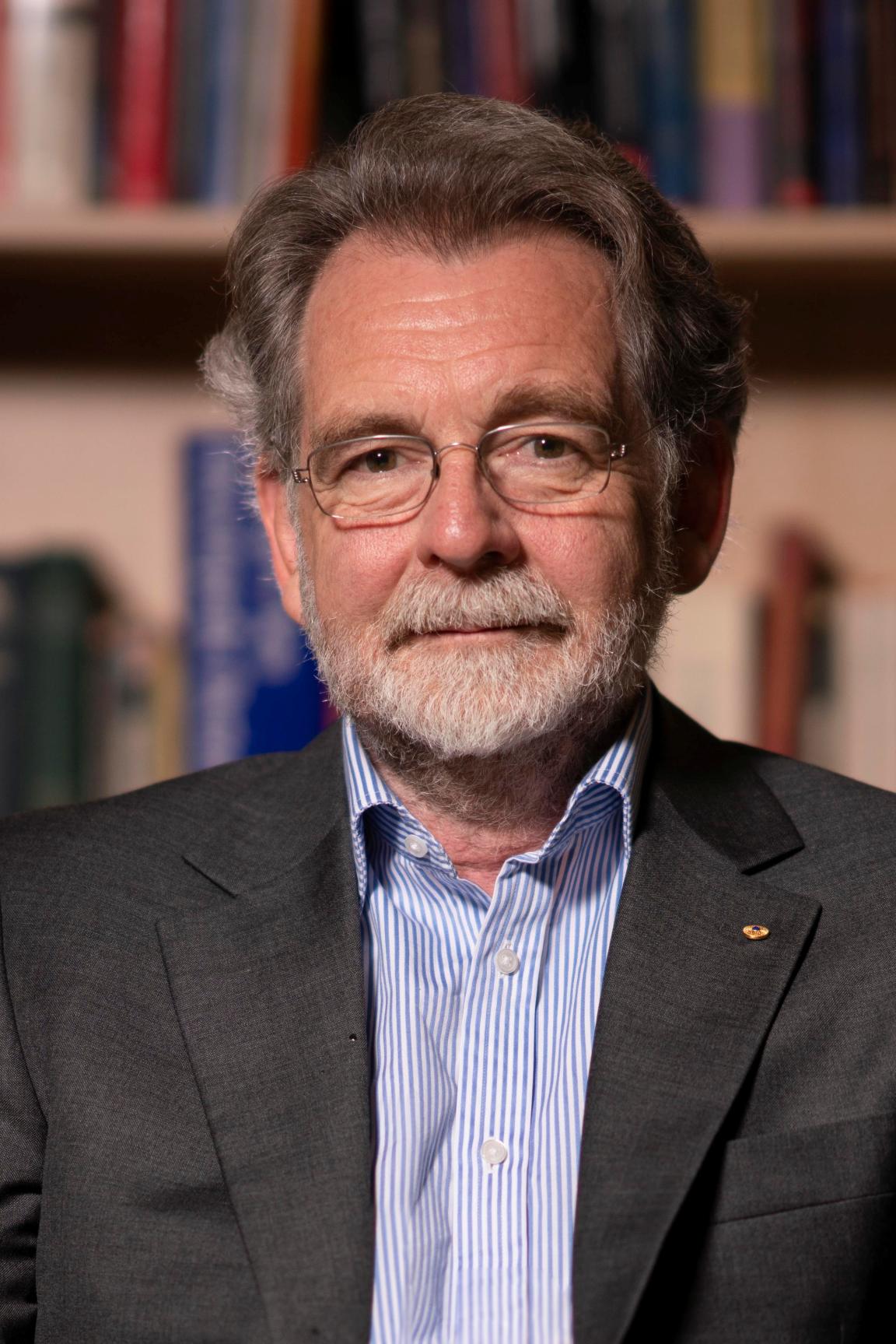 A portrait of a bearded man wearing a blue shirt and black jacket
