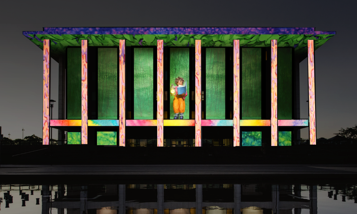 A colourful projection on the National Library of Australia building featuring a figurine reading a book while holding a lamp