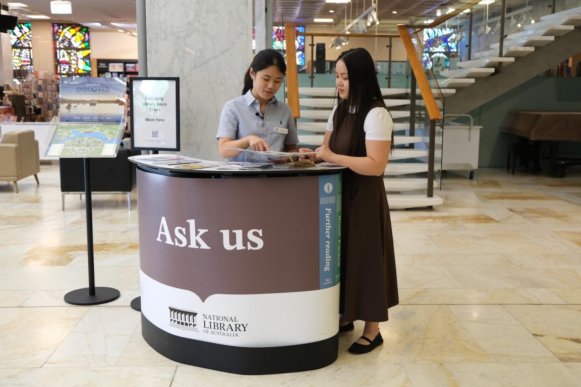 Young Library volunteer standing behind the meet and greet desk assisting a visitor