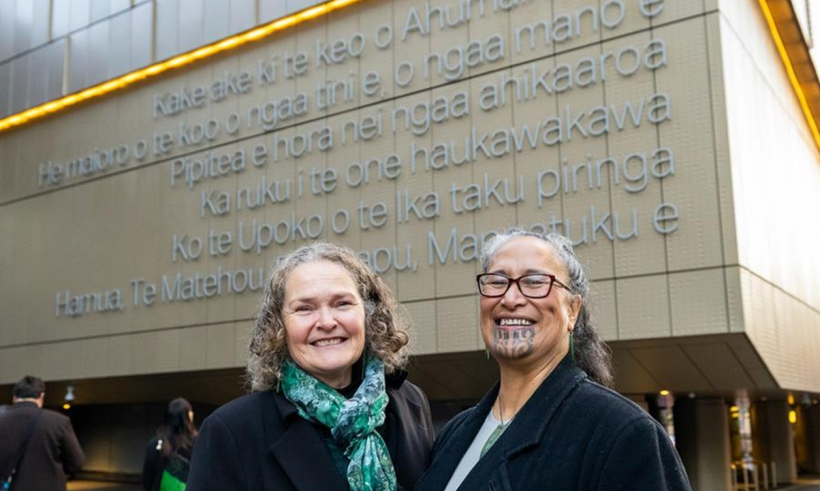 Two smiling women pictured at the front of the Archives New Zealand building
