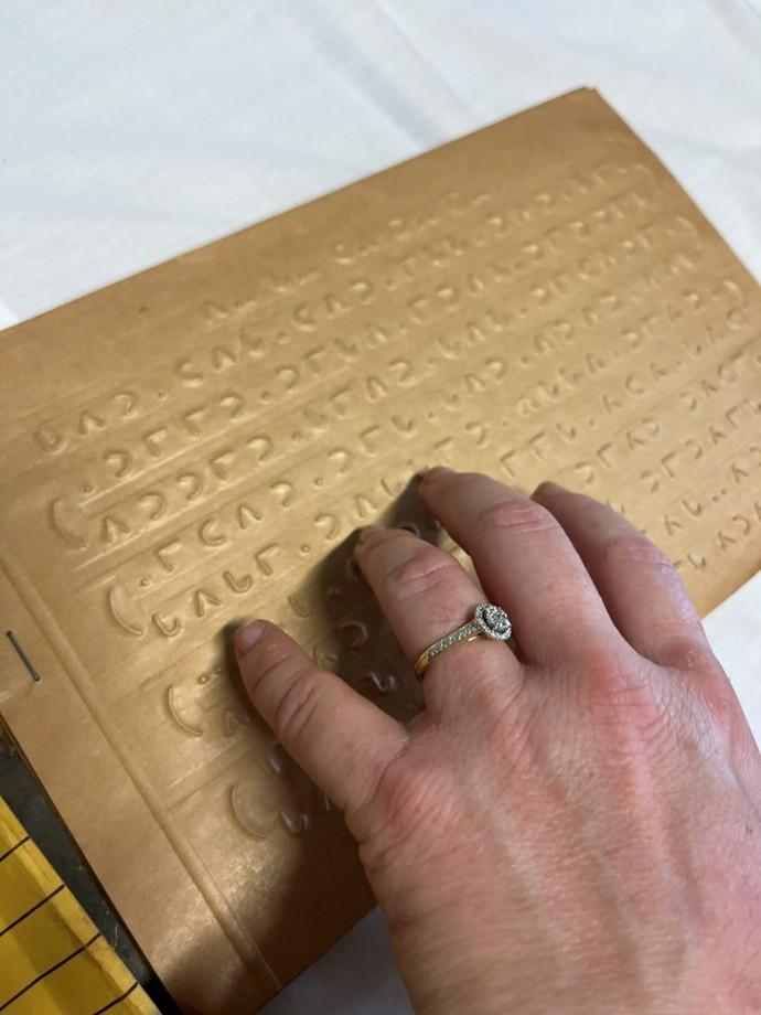 A person’s hand sits on a book written in braille