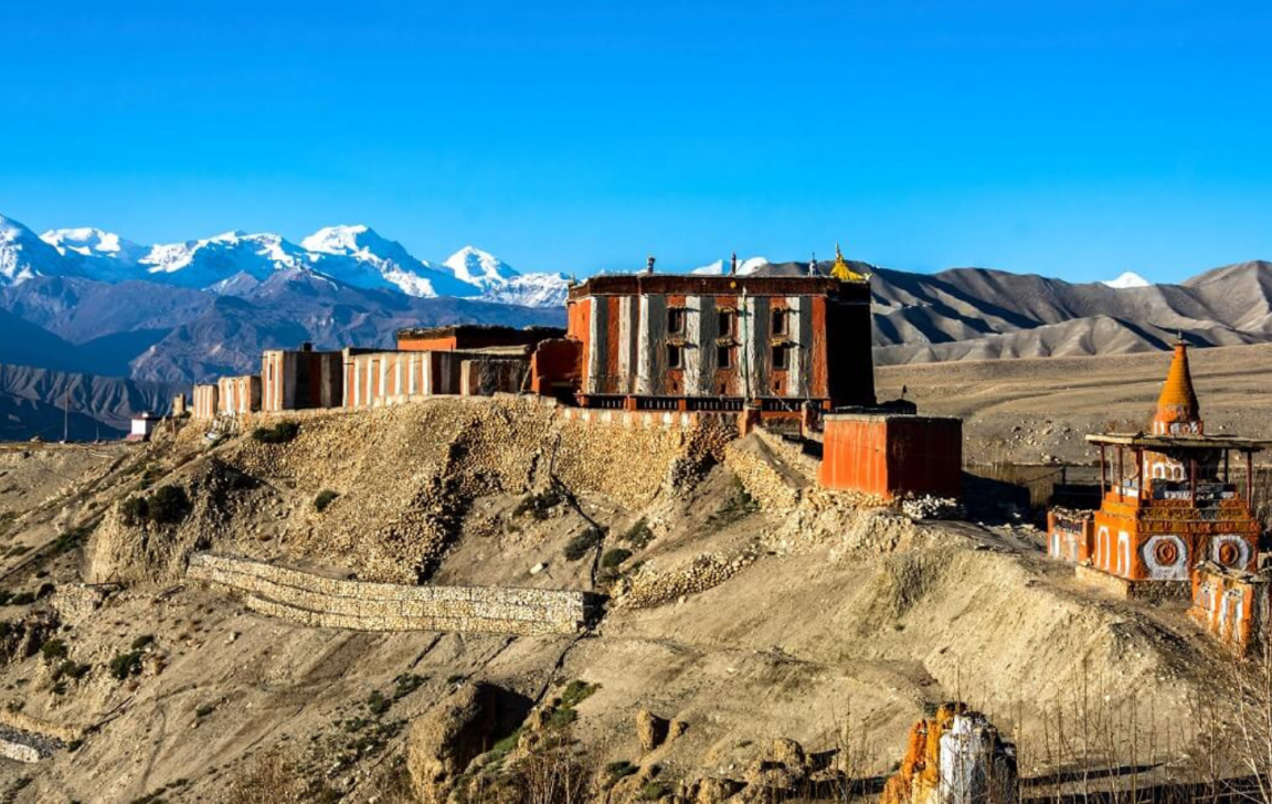 A monastery and other buildings with mountains with snow on top in the background