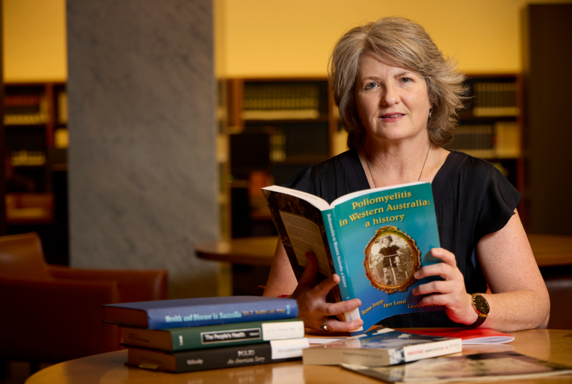 A headshot of a woman holding a blue book in the National Library's Main Reading Room